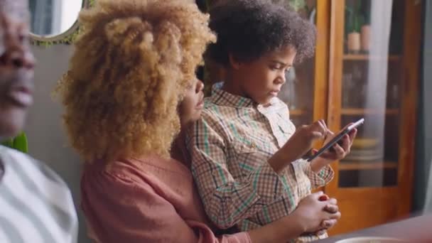 Petit garçon afro-américain assis avec sa mère et jouant sur une tablette numérique pendant le dîner familial à la maison - Séquence, vidéo