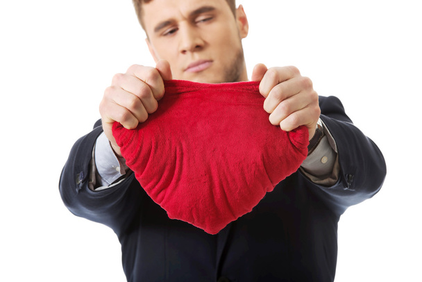 Businessman tears heart shaped pillow. - Фото, изображение