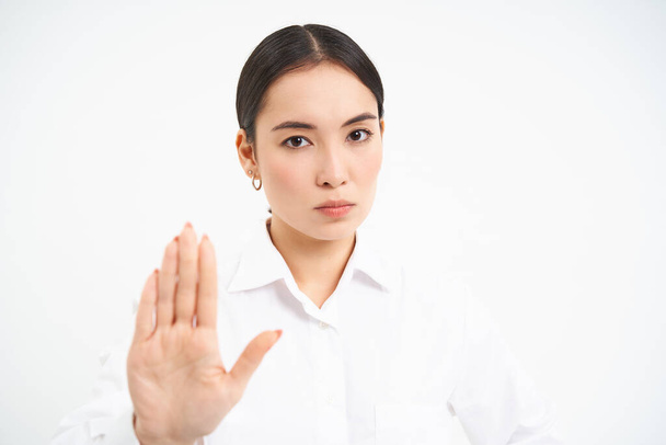 もうやめてください。深刻なアジアの女性管理者は、ビジネスの女性は、手のジェスチャーを拡張し、不承認を示し、笑顔、白い背景を禁止します. - 写真・画像