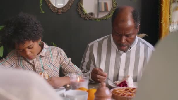Afroamerykanka matka, ojciec i mały syn jedzą słodkie ciasto i rozmawiają z rodziną podczas urodzinowej kolacji - Materiał filmowy, wideo