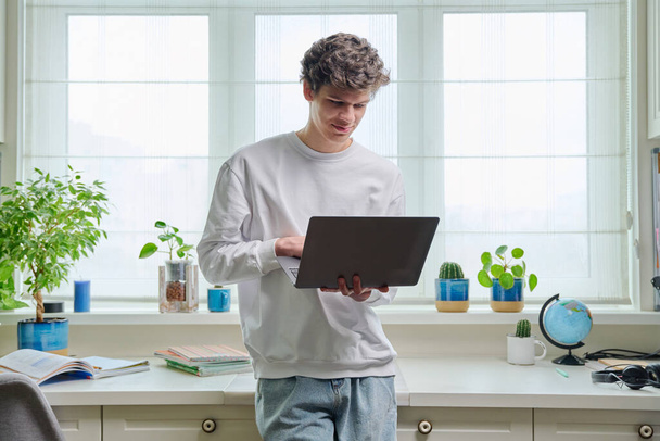 Retrato de amigável jovem estudante universitário cara segurando laptop, em casa interior. Bonito homem 18-20 anos de idade usando laptop. Tecnologias de internet on-line estudo remoto e-learning comunicação de lazer - Foto, Imagem
