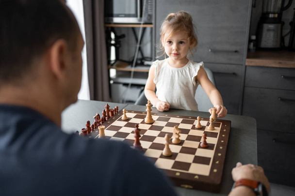 Father teaching his little daughter to play chess at the table in home kitchen. The concept early childhood development and education. Family leisure, communication and recreation. High quality photo - Fotoğraf, Görsel
