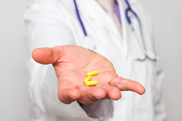 Close-up da mão de um médico caucasiano irreconhecível segurando três pílulas amarelas. - Foto, Imagem