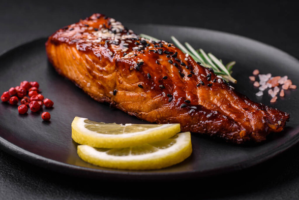 Delicious grilled red salmon fish with sauce, sesame seeds, spices and herbs on a dark concrete background - Foto, Bild
