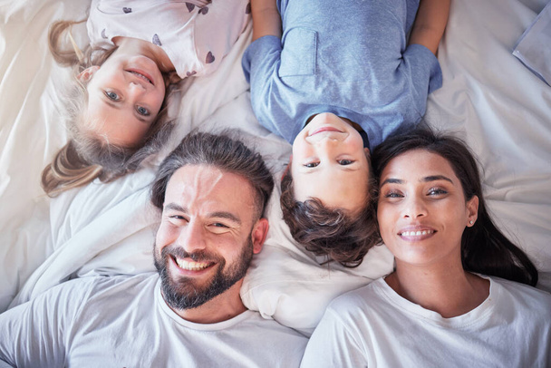 Top view, smile and family on bed, love and bonding with quality time, break and relax together. Portrait, happy parents and mother with father, children and siblings in bedroom, happiness and peace. - 写真・画像