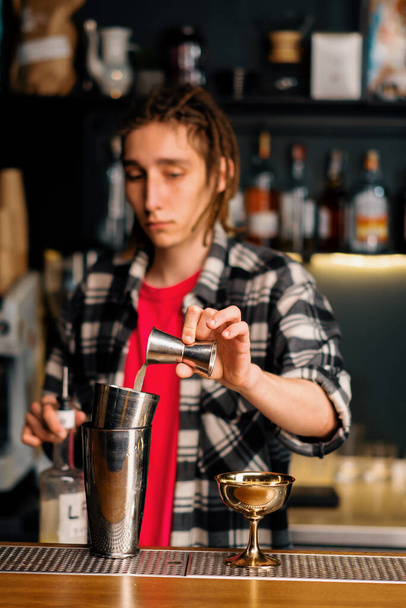 An experienced bartender pours liquid into a shaker with the help of a jigger prepares a cocktail in night club - Photo, Image