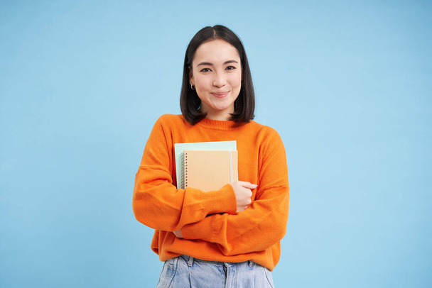 Sorridente donna asiatica con quaderni, studente con il viso felice, promo di istruzione universitaria, sfondo blu. - Foto, immagini
