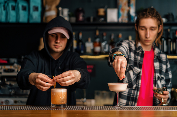 два молодых бармена готовят алкогольные коктейли в баре, смешивая ингредиенты, работая парами на вечеринке - Фото, изображение