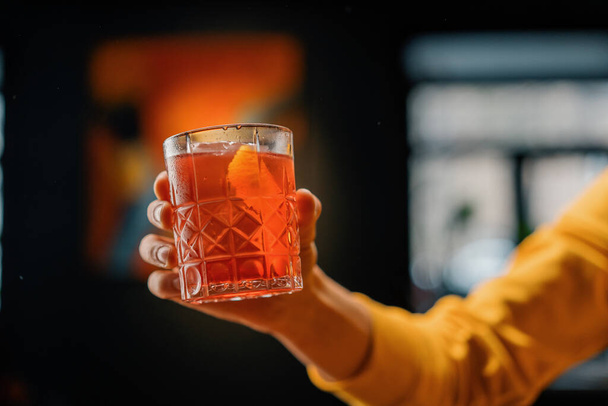 Close-up of a bar guest holding ready-made delicious Negroni alcoholic cocktail in his hand - Фото, изображение