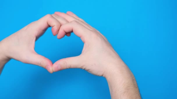 A young mans hand makes a heart with two hands on a blue background. Hand gesture on a blue background. A gesture of love. - Footage, Video