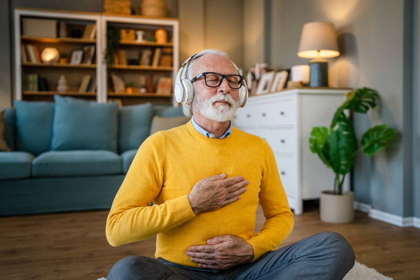 um homem maduro masculino caucasiano usando fones de ouvido para meditação guiada on-line praticando mindfulness ioga manifestação com os olhos fechados em casa pessoas reais autocuidado conceito espaço de cópia - Foto, Imagem