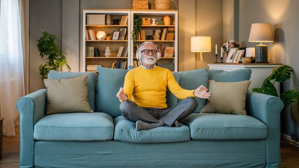 egy férfi érett idősebb kaukázusi férfi használja fejhallgató az online vezetett meditáció gyakorlása éberség jóga megnyilvánulása a szemét csukott otthon valós emberek öngondoskodás koncepció másolás tér - Fotó, kép