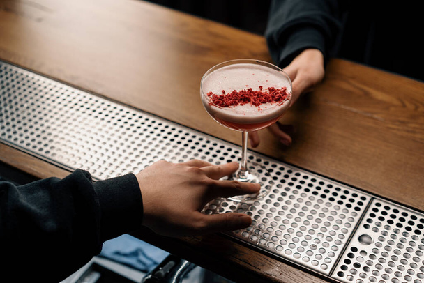 the bartender gives a delicious pink freshly prepared raspberry milk punch cocktail to the client from bar counter - Photo, image