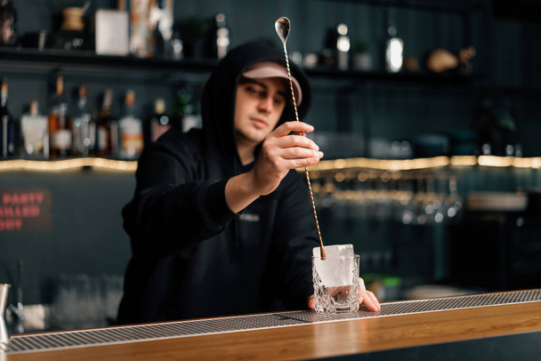 profesjonalny barman mieszający kostki lodu z długą łyżką za barem młody człowiek przygotowujący świeży koktajl - Zdjęcie, obraz