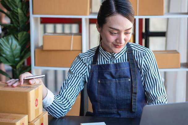 Azjatka bizneswoman cieszy się swoją działalnością internetową MŚP, sprzedając produkty, czerpiąc korzyści z otwarcia sklepu internetowego i przyjmując zamówienia na paczki klientów wewnątrz biura. Koncepcja działalności MŚP. - Zdjęcie, obraz