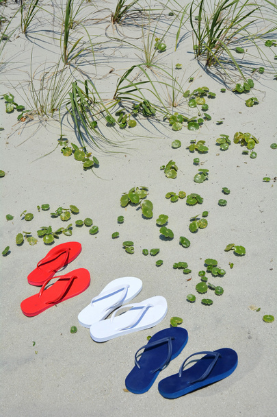 Tongs rouges blanches et bleues sur le sable parfait pour l'art de la couverture
 - Photo, image