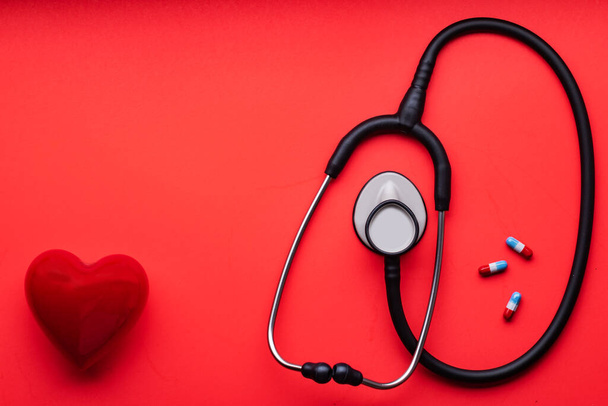 medical stethoscope, red heart and pills on a red background. View from above. Space for text - Photo, Image