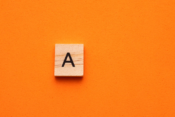 Alphabet letter A on wooden square tile - Orange foamy background - Fotó, kép