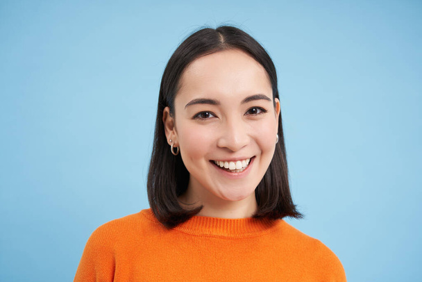 Közelkép portré gyönyörű koreai nő egészséges mosollyal, természetes tiszta arc bőr, áll a kék háttér. - Fotó, kép