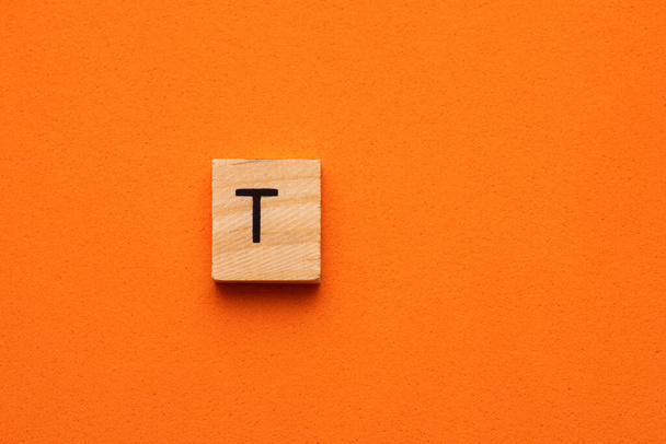 Alphabet capital letter T on wooden square tile - Orange foamy background - Fotó, kép