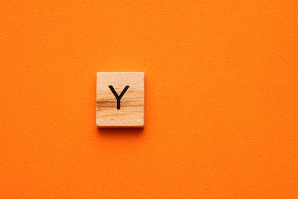 Alphabet letter Y on wooden square tile - Orange foamy background - 写真・画像