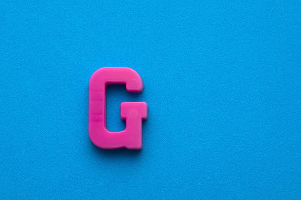 Plastic pink letter G uppercase on blue foamy background - Fotoğraf, Görsel