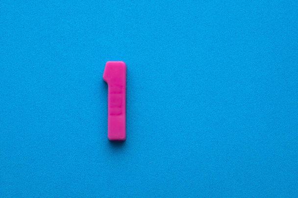 Number 1 color pink - Plastic piece on blue foamy background - Photo, image