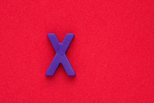 Alphabet letter X - Violet colored plastic piece on red 032 c foamy background - Foto, Imagem