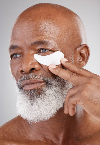 Hautpflege, Kollagen-Augenmaske und schwarzer Mann mit Hand auf Gesicht auf Studiohintergrund für eine professionelle Anti-Aging-Wellness-Behandlung. Dermatologie, kosmetischer Prozess und ausgereiftes Modell mit Hautpflege für die Augen - Foto, Bild