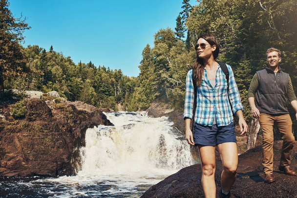 Mantente salvaje. una joven pareja caminando junto a un río rocoso y una cascada - Foto, Imagen