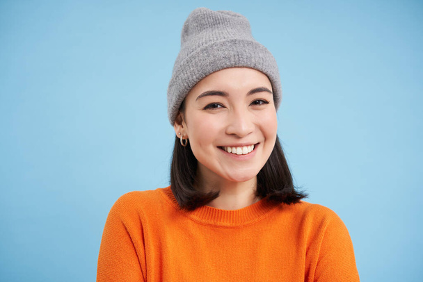 Gros plan portrait de sourire, belle jeune femme, fille asiatique en chapeau, regardant heureux et franc à la caméra, debout sur fond bleu. - Photo, image