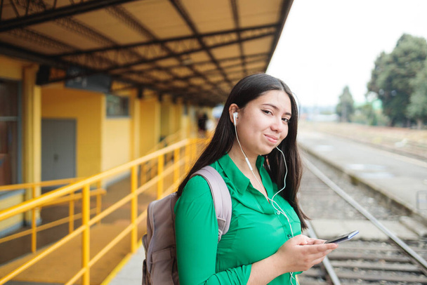 Intrattenimento on-the-Go: giovane donna in stazione utilizzando la tecnologia mobile per trasmettere film e connettersi sui social media. Foto di alta qualità - Foto, immagini