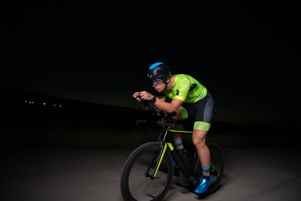 A triathlete rides his bike in the darkness of night, pushing himself to prepare for a marathon. The contrast between the darkness and the light of his bike creates a sense of drama and highlights the - Fotó, kép
