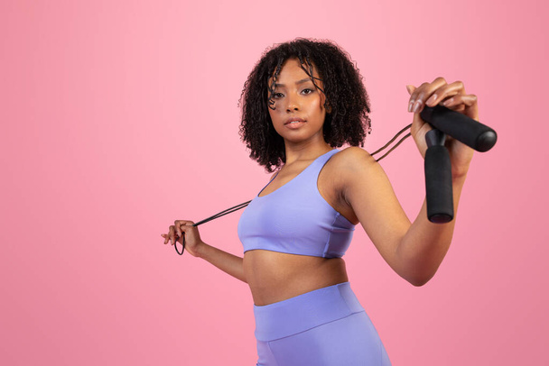 Serious confident millennial african american lady in sportswear doing hand exercises with dumbbells isolated on pink studio background. Cardio workout, muscle training, sport, fit and body care - Photo, Image