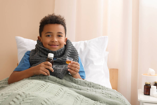 African-American boy taking cough syrup on bed at home, space for text. Cold medicine - Zdjęcie, obraz