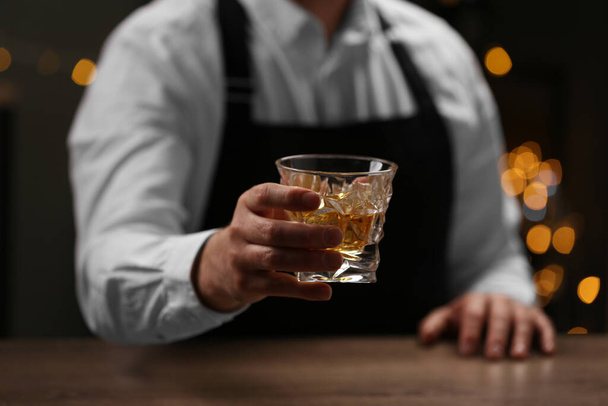 Bartender with glass of whiskey at bar counter indoors, closeup - Foto, Imagem
