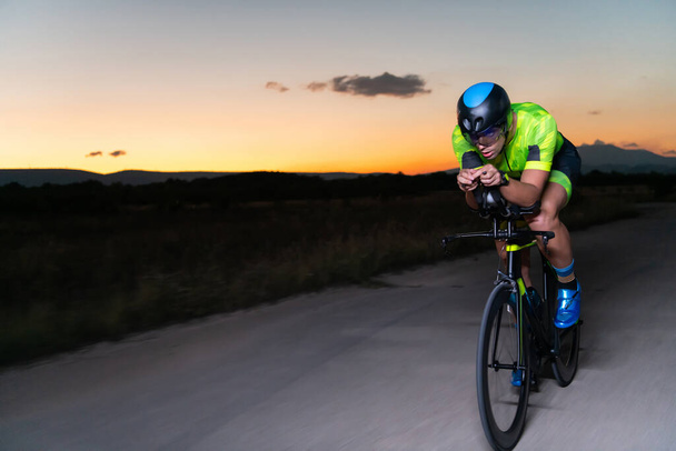 A triathlete rides his bike in the darkness of night, pushing himself to prepare for a marathon. The contrast between the darkness and the light of his bike creates a sense of drama and highlights the - Foto, afbeelding