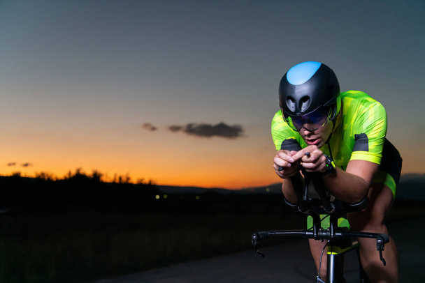 A triathlete rides his bike in the darkness of night, pushing himself to prepare for a marathon. The contrast between the darkness and the light of his bike creates a sense of drama and highlights the - Фото, изображение
