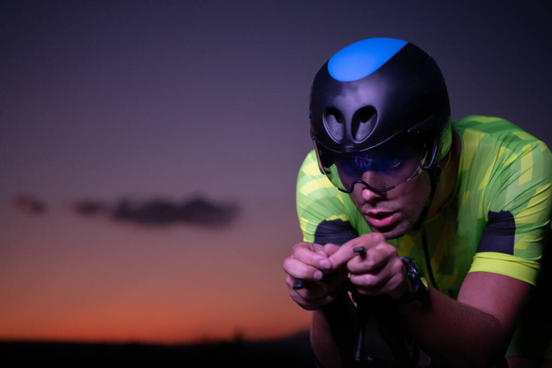 A triathlete rides his bike in the darkness of night, pushing himself to prepare for a marathon. The contrast between the darkness and the light of his bike creates a sense of drama and highlights the - Photo, Image