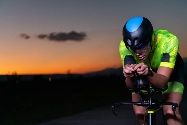 A triathlete rides his bike in the darkness of night, pushing himself to prepare for a marathon. The contrast between the darkness and the light of his bike creates a sense of drama and highlights the - Фото, изображение