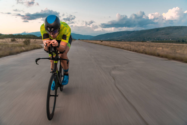  Gün batımında bisiklet süren bir triatloncu, maratona hazırlanıyor. Gökyüzünün sıcak renkleri kararlı ve odaklanmış çabaları için güzel bir zemin sağlar. - Fotoğraf, Görsel