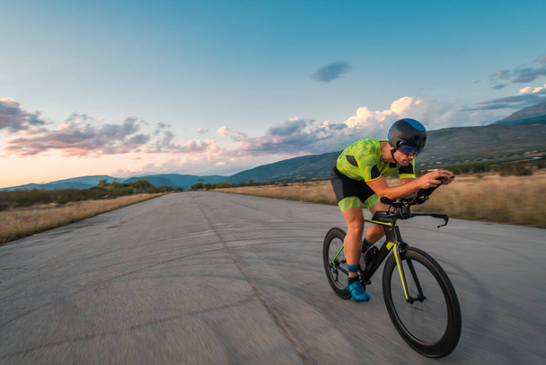  Triathlete riding his bicycle during sunset, preparing for a marathon. The warm colors of the sky provide a beautiful backdrop for his determined and focused effort - Фото, зображення