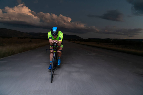 A triathlete rides his bike in the darkness of night, pushing himself to prepare for a marathon. The contrast between the darkness and the light of his bike creates a sense of drama and highlights the - Fotoğraf, Görsel