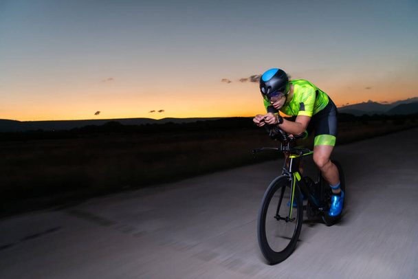 A triathlete rides his bike in the darkness of night, pushing himself to prepare for a marathon. The contrast between the darkness and the light of his bike creates a sense of drama and highlights the - Valokuva, kuva