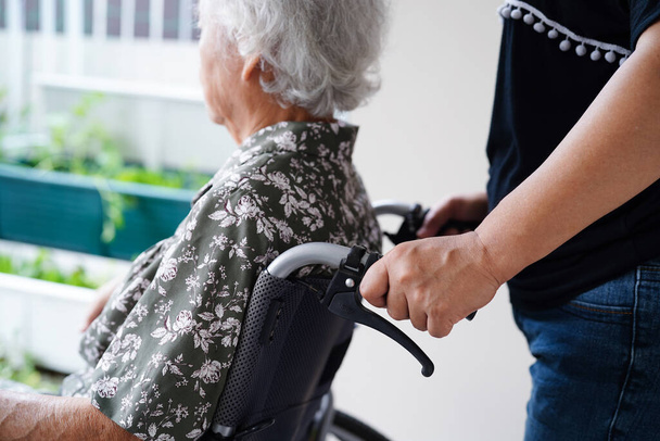 Bakıcı, hastanede tekerlekli sandalyede oturan Asyalı yaşlı kadın maluliyet hastasına yardım ediyor.. - Fotoğraf, Görsel