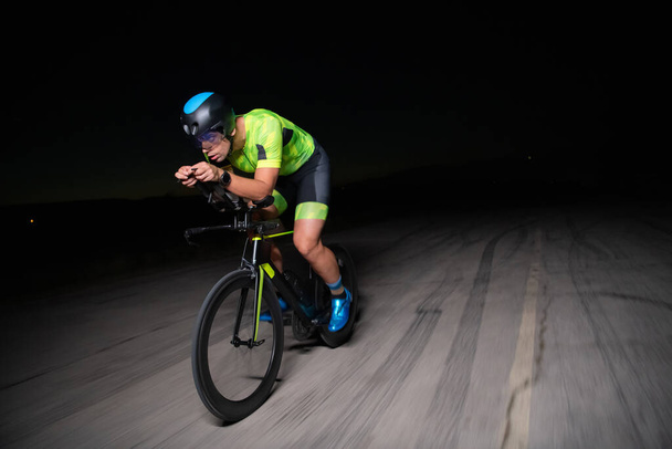 A triathlete rides his bike in the darkness of night, pushing himself to prepare for a marathon. The contrast between the darkness and the light of his bike creates a sense of drama and highlights the - Фото, зображення