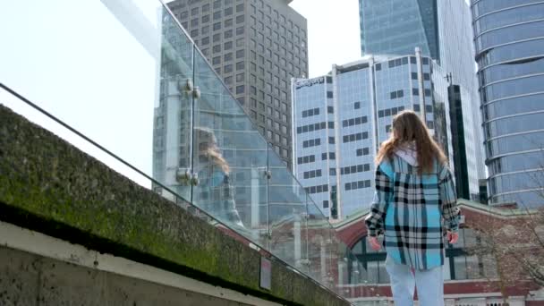 teenager dívka kráčí podél náspu na pozadí mrakodrapy obrovských skleněných budov zpět dívka jde daleko zastávky a dívá se na přírodu Vancouver Canada Place Harbor Center - Záběry, video