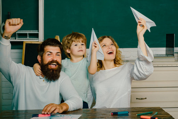 Pupil with paper airplane playing with parents. Young couple helping his son to make homework. Parent taking child to school. Parents feeling proud on progress of son. Parenting Education mathematics - Φωτογραφία, εικόνα