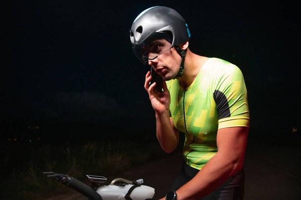 Egy triatlonos okostelefont használ, miközben szünetelteti a kemény éjszakai kerékpáros edzést. Kiváló minőségű fénykép - Fotó, kép