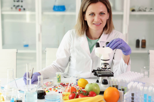 Chemist with microscope improves vitamin and mineral capsules in laboratory. Experiments comparing fresh vegetables and fruits with capsules - Foto, imagen